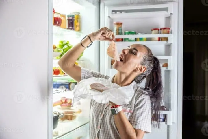 Very hungry woman in pajamas enjoying ham at night by the fridge photo